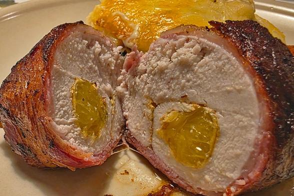 Baconlindad apelsinkyckling med jalapeño i genomskärning, i bakgrunden syns en potatisgratäng.