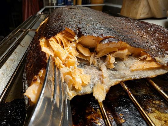 En varmrökt laxsida där någon tjuvat till sig smakbitar så det saftiga rosa köttet syns under den rökta, mörka ytan.