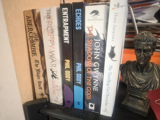 A row of books, from left to right: Joe Abercrombie "The Blade itself", R. F. Kuang "The Poppy Wars", Phil Oddy "Entrapment, Phil Oddy Echoes, John Gwynne "The shadow of the gods", and Hiro Arikawa "The travelling cat chronicles"

