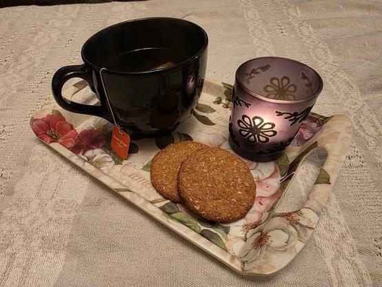 A cup of tea, two hobnobs, and a lit candle on a pretty little tray.