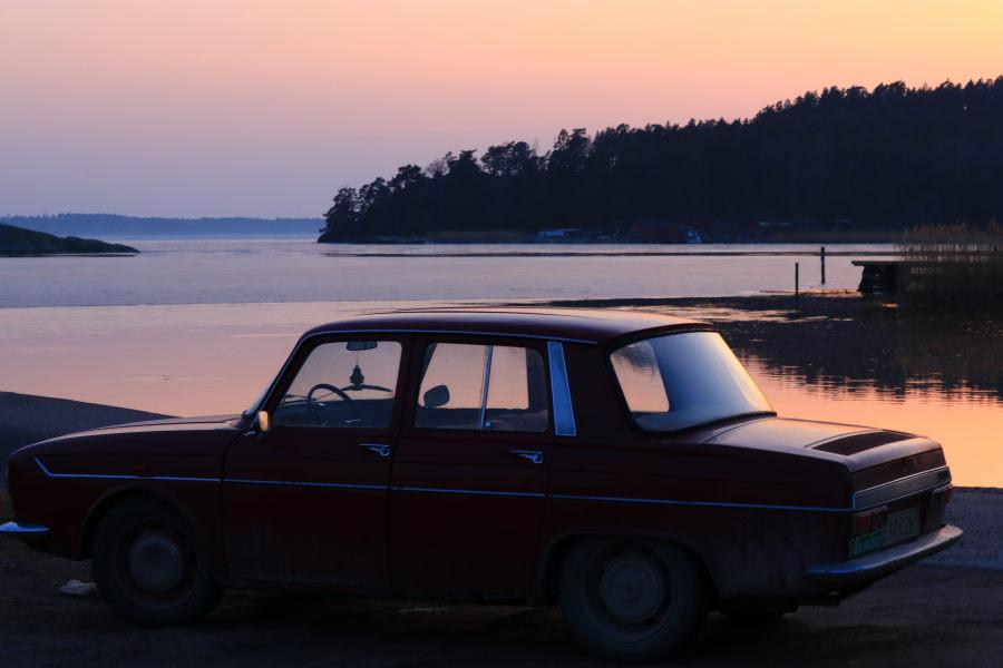 An old and a bit chabby Renault 10 (1965-68?) standing by the shore one evening just after sunset. The sky and sea has both warm and cold colours but the forest in the distance is only seen as a silhouette.