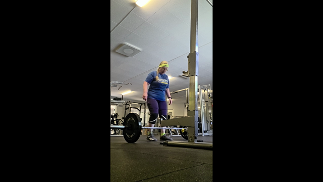 En video från ett standard-gym med en kvinna i övre medelåldern som gör sumo-marklyft för första gången. 