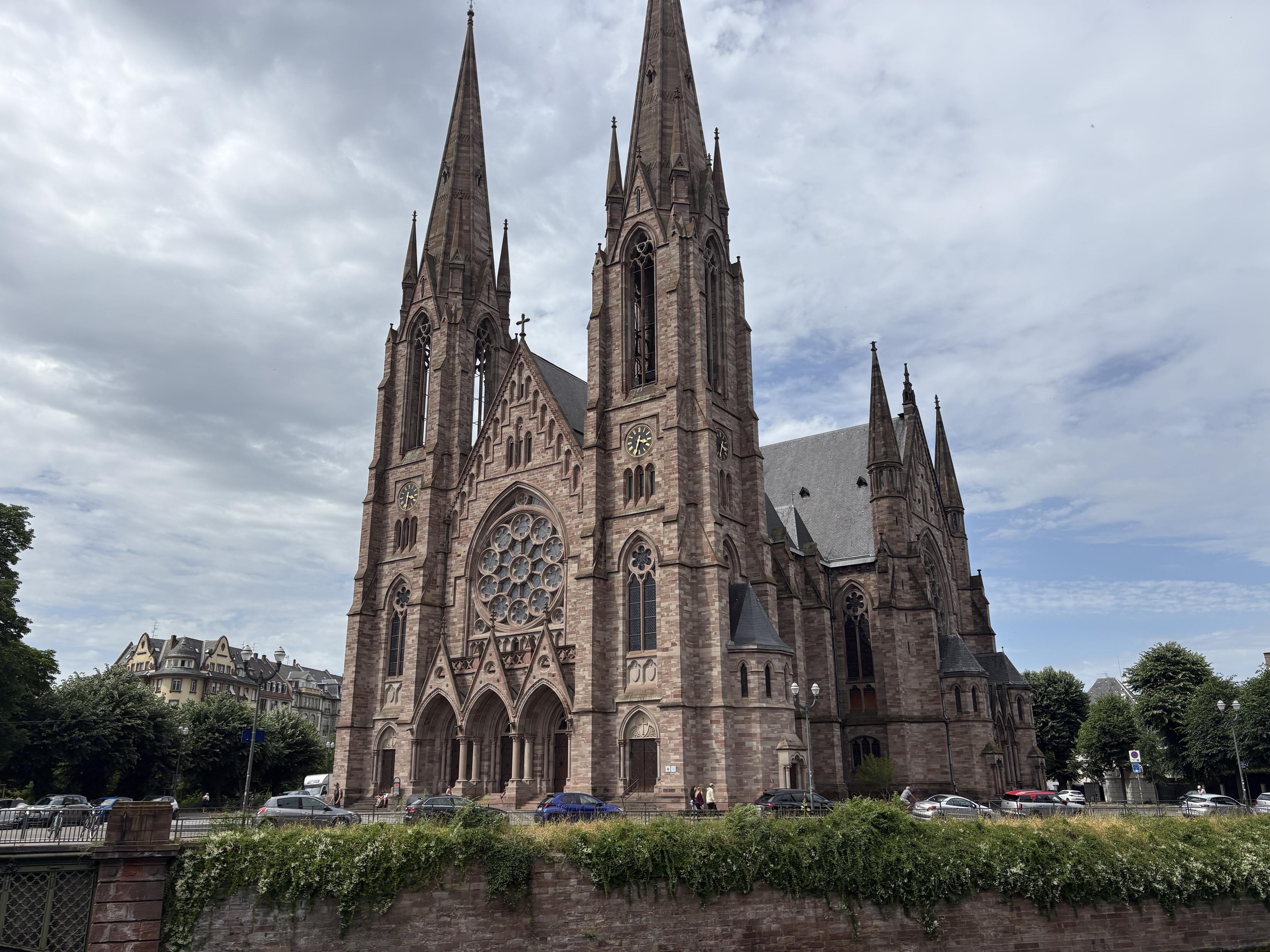 Vista frontal y lateral de la iglesia, con el gran rosetón sobre el pórtico de entrada, franqueada con las dos torres. En el lateral se ve también el transepto. En la parte inferior, el río.
