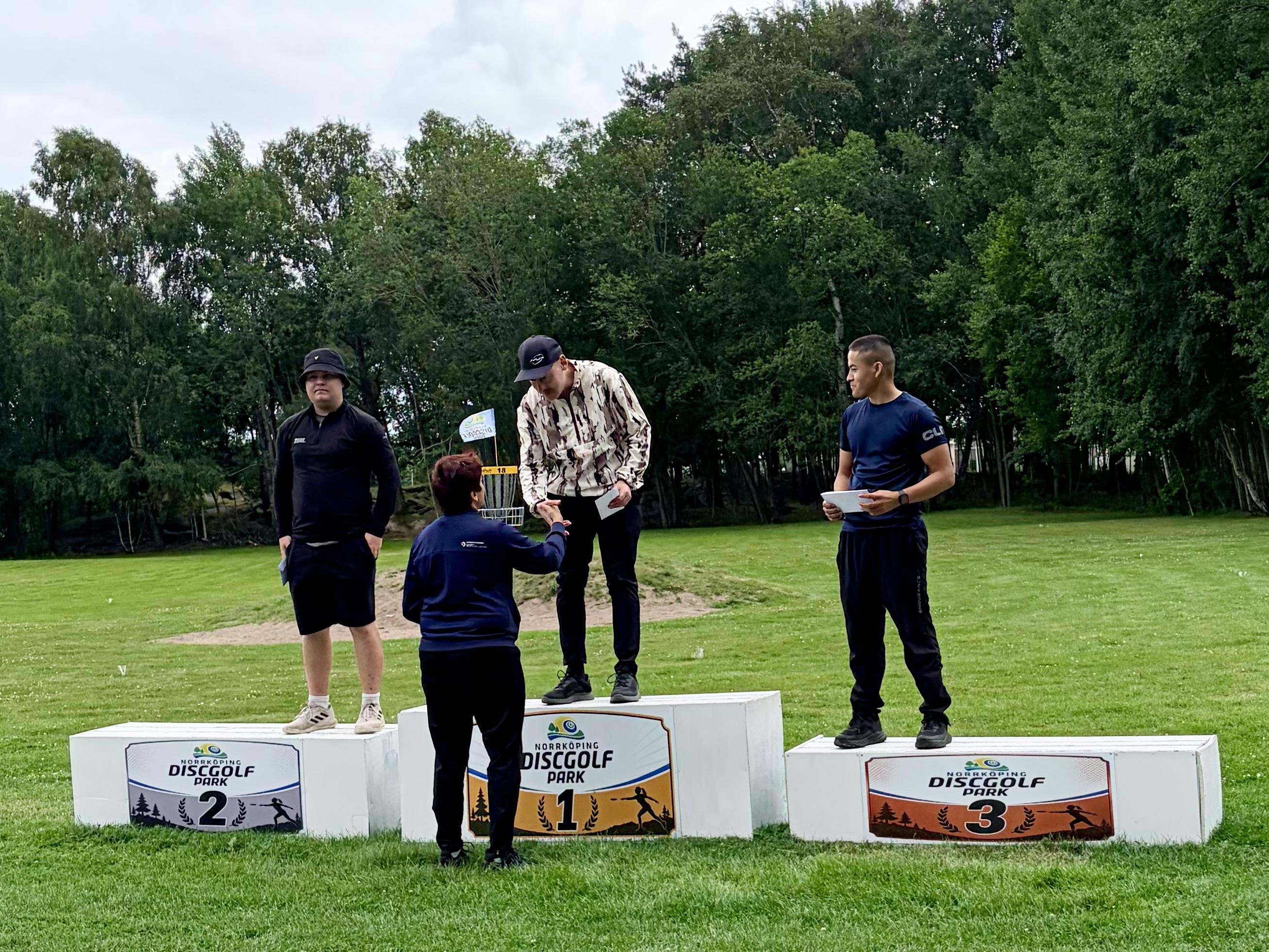 3 men on a podium, me on the top spot shaking hands with the tournament director
