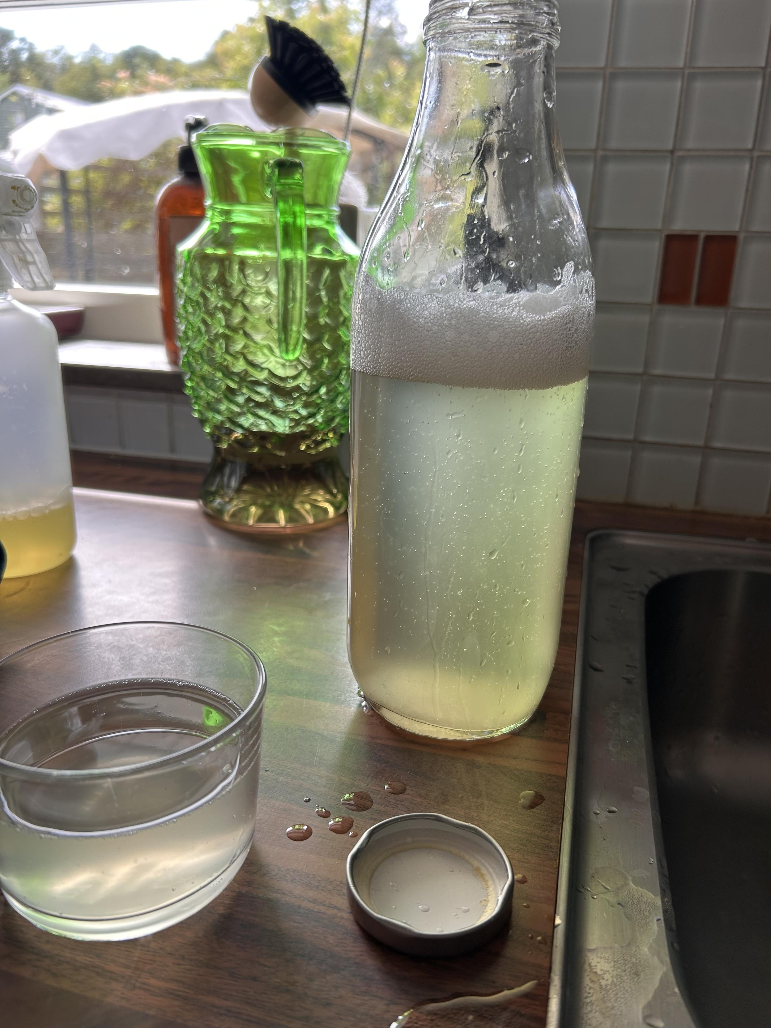 En öppnad flaska med bubbligt innehåll på en diskbänk. Bredvid står ett glas.